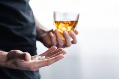 partial view of depressed man with glass of whiskey and handful of pills
