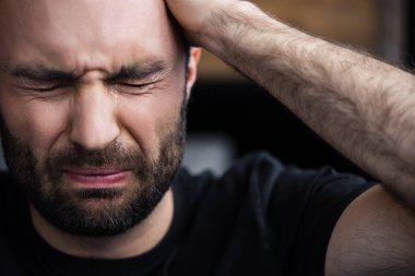 depressed bearded man crying with closed eyes and holding hand on head clipart