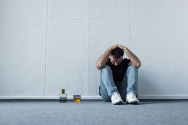 depresif adam şişe ve viski cam yakınında beyaz duvar tarafından katta oturan