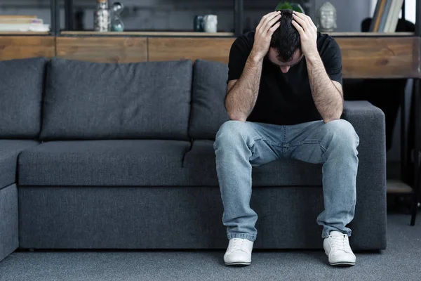 Sad Adult Man Blue Jeans Sitting Grey Sofa Holding Hands — Stock Photo, Image