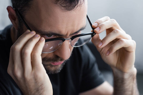 Красивый серьезный небритый мужчина, отводящий взгляд и трогающий очки
 