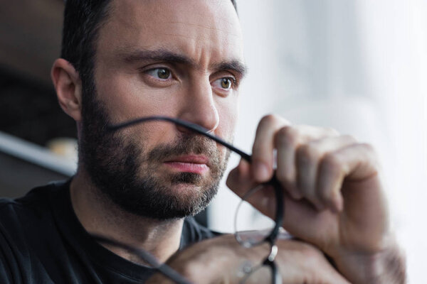 селективный фокус задумчивого бородатого мужчины, держащего очки и отворачивающегося
