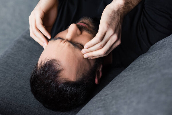 overhead view of man lying with closed eyes and holding hands near head