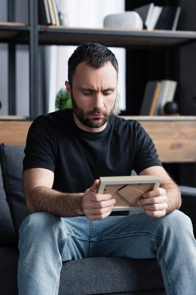 Aufgebrachter Gutaussehender Bärtiger Mann Sitzt Auf Sofa Und Hält Fotorahmen — Stockfoto