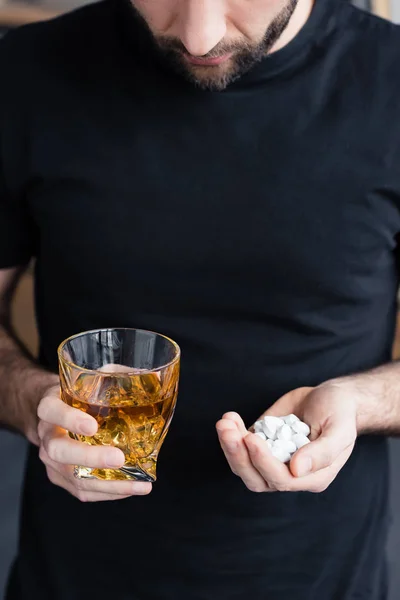 ウイスキーのグラスと錠剤の一握りを保持する黒いTシャツの立っている男の部分的なビュー — ストック写真