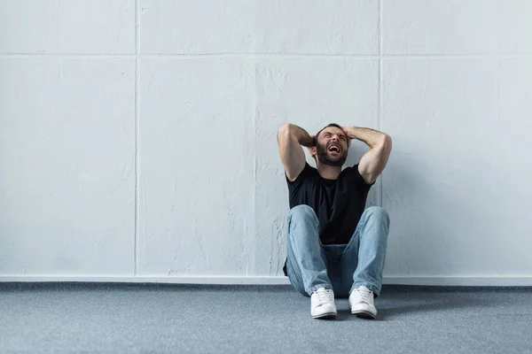 Дорослий Депресивний Чоловік Кричить Сидячи Підлозі Біля Білої Стіни — стокове фото