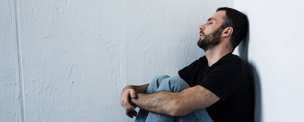 panoramic shot of suffering man sitting in corner and looking away