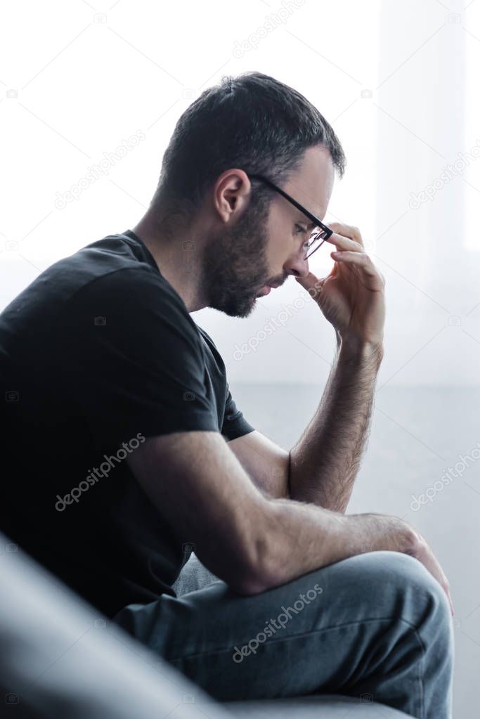 selective focus of sad bearded man in glasses holding hand near face