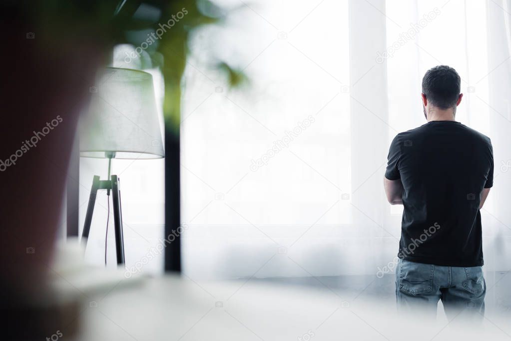 selective focus of short haired man in black t-shirt standing by window at home