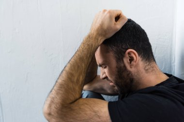 sakallı depresif adam beyaz duvarın yanında duran ve baş el ele tutuşarak