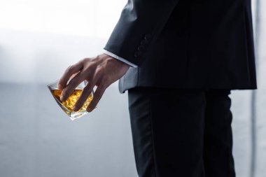 partial view of man in black suit holding glass of whiskey clipart