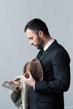 elinde şapka tutarken çerçeve içinde fotoğraf bakarak takım elbiseli depresif adam