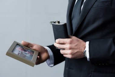 çerçeve içinde şişe ve fotoğraf tutan takım elbiseli adamın kırpılmış görünümü 