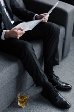 katta viski bardağının yanında gazete ile kanepede oturan işadamı