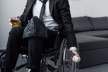 top ve viski cam tutarken diz üzerinde çanta ile tekerlekli sandalyede oturan engelli adamın kısmi görünümü