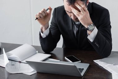 boş ekranlı dizüstü bilgisayar, belgeler ve akıllı telefon yakınında işyerinde oturan düşünceli işadamı
