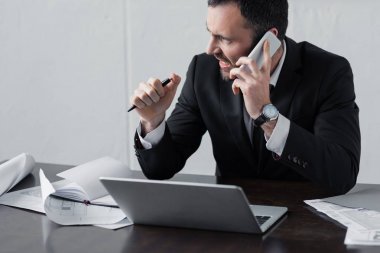 işyerinde otururken akıllı telefon konuşurken siyah takım elbiseli işadamı memnun değil 