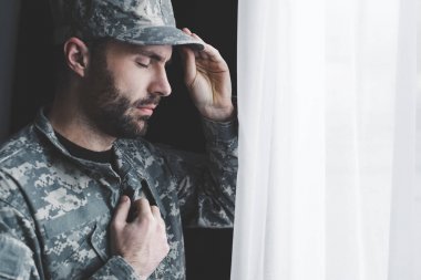 kapalı gözlerle pencerenin yanında dururken göğsünde el tutan üniformalı pensive sakallı adam