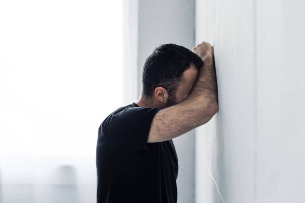 adult depressed man in black t-shirts standing near white wall at home