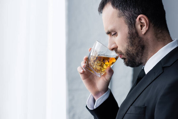 side view of frustrated, handsome bearded man drinking whiskey