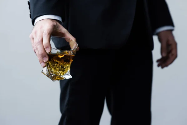 ウイスキーのグラスを持つ黒いスーツを着た大人の男のトリミングされた眺め — ストック写真