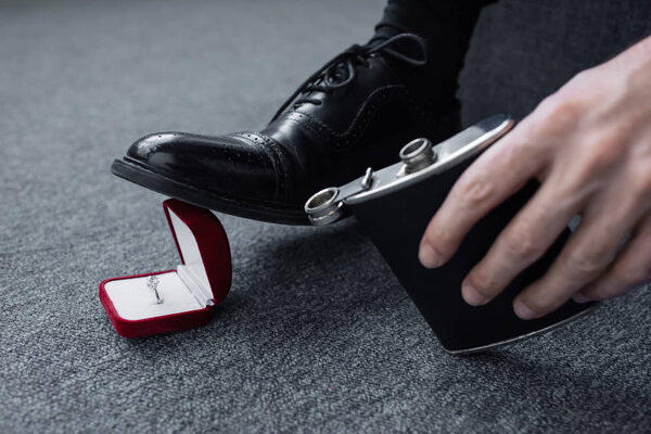 cropped view of man holding flask and trampling gift box with ring