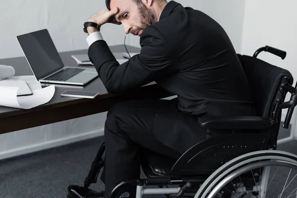 坐在轮椅上 手牵着额头的残疾商人 心烦意乱地坐在工作场所 — 图库照片
