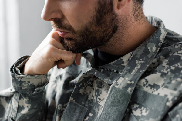 partial view of bearded military man in uniform holding hand near face