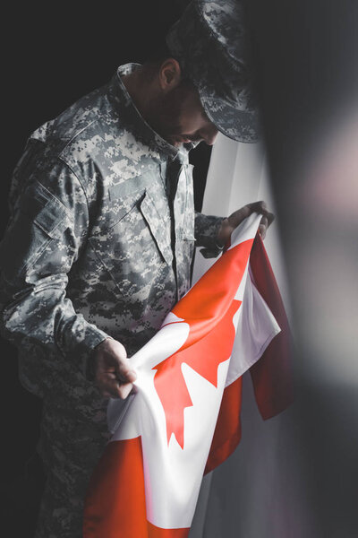 selective focus of depressed man in military uniform holding canada national flag 