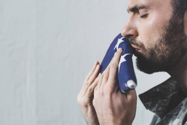 красивый небритый военный, целующий национальный флаг США с закрытыми глазами
