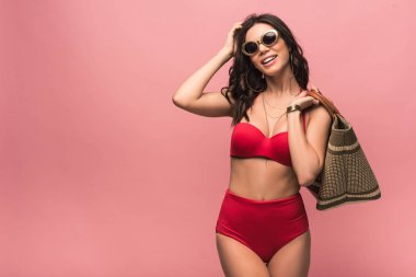pembe izole plaj çantası tutan mayo ve güneş gözlüğü gülümseyen çekici kadın