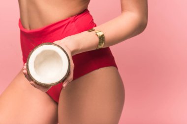 cropped view of woman in panties holding cut coconut isolated on pink clipart