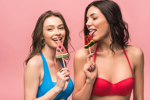 two pretty girls in bikini eating watermelon lollipops isolated on pink