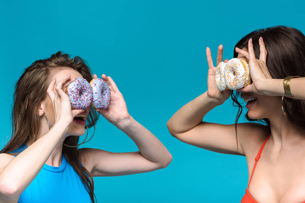 Две девушки в купальниках, держащие пончики изолированные на голубом

