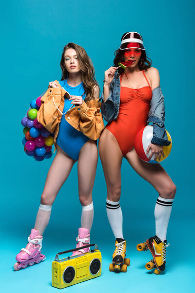 full length view of two stylish girls in roller skates eating armelon lollipop on blue
