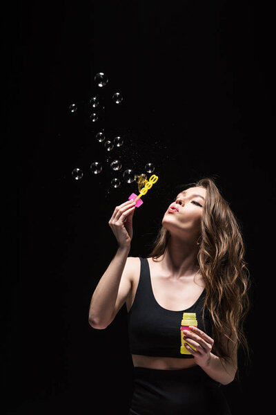 pretty young woman blowing soap bubbles isolated on black