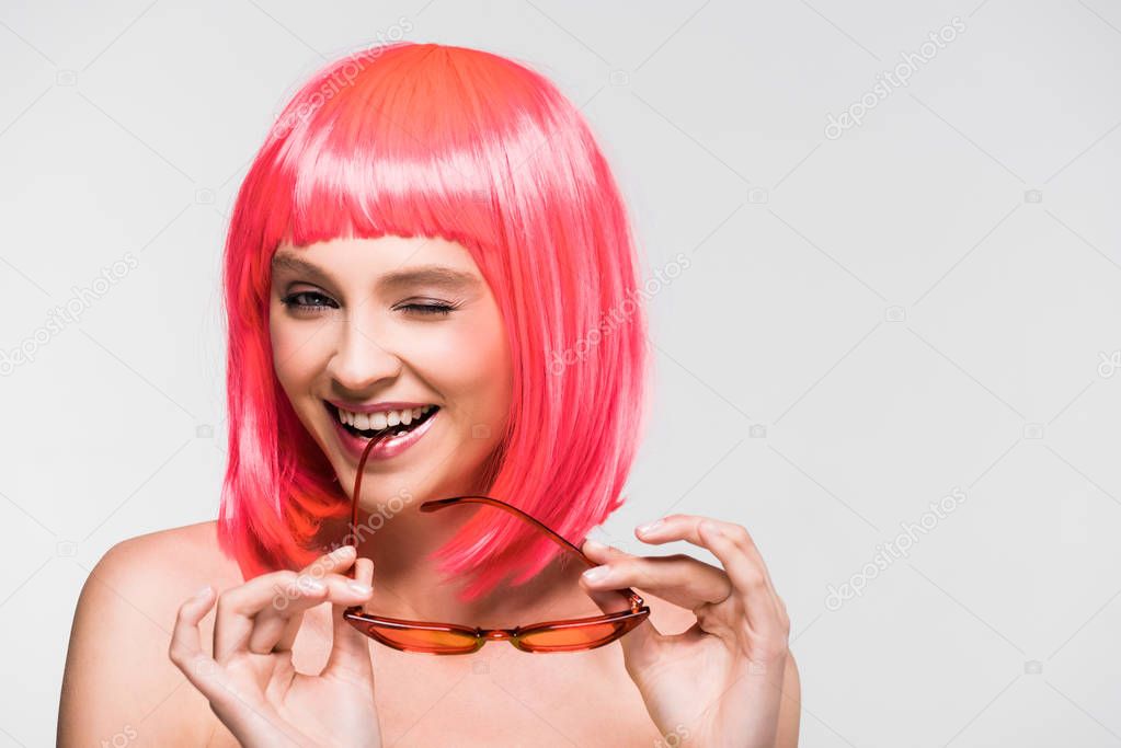 pretty girl winking in pink wig and trendy sunglasses isolated on grey