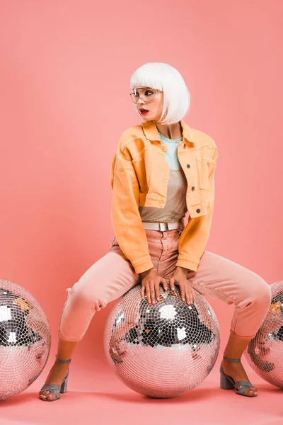 stylish model in white wig posing with disco balls on pink