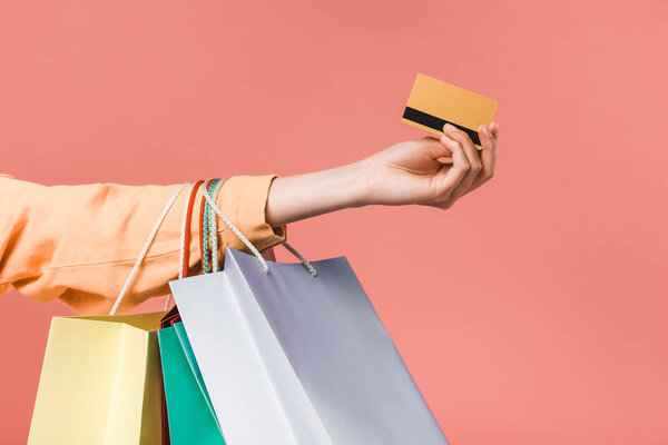 partial view of woman with shopping bags and credit card, isolated on pink