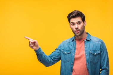 surprised handsome man pointing with finger isolated on yellow clipart