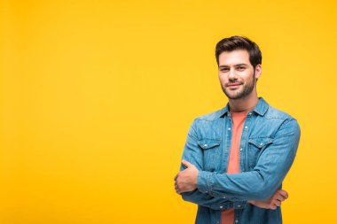 happy handsome man with crossed arms looking at camera isolated on yellow clipart