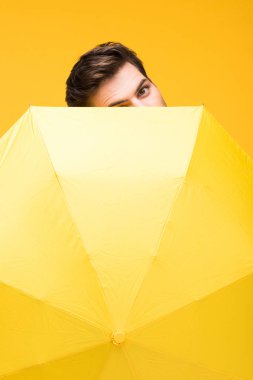 handsome man covering face with umbrella isolated on yellow clipart