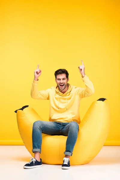 黄色の指で指を指す豆袋の椅子の興奮した男 — ストック写真