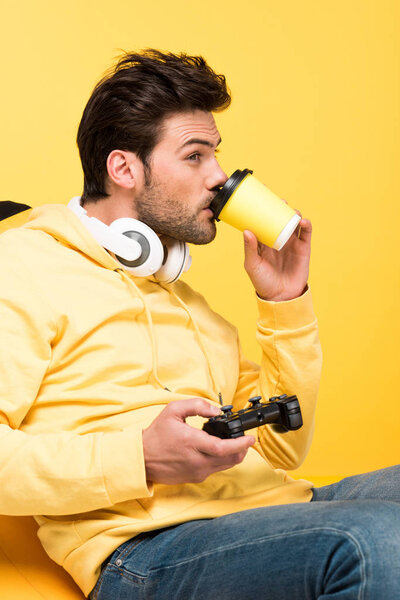 KYIV, UKRAINE - APRIL 12: man drinking coffee to go and playing Video Game isolated on yellow