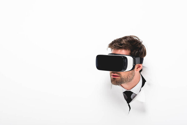 man in Virtual reality headset behind hole in wall on white with copy space