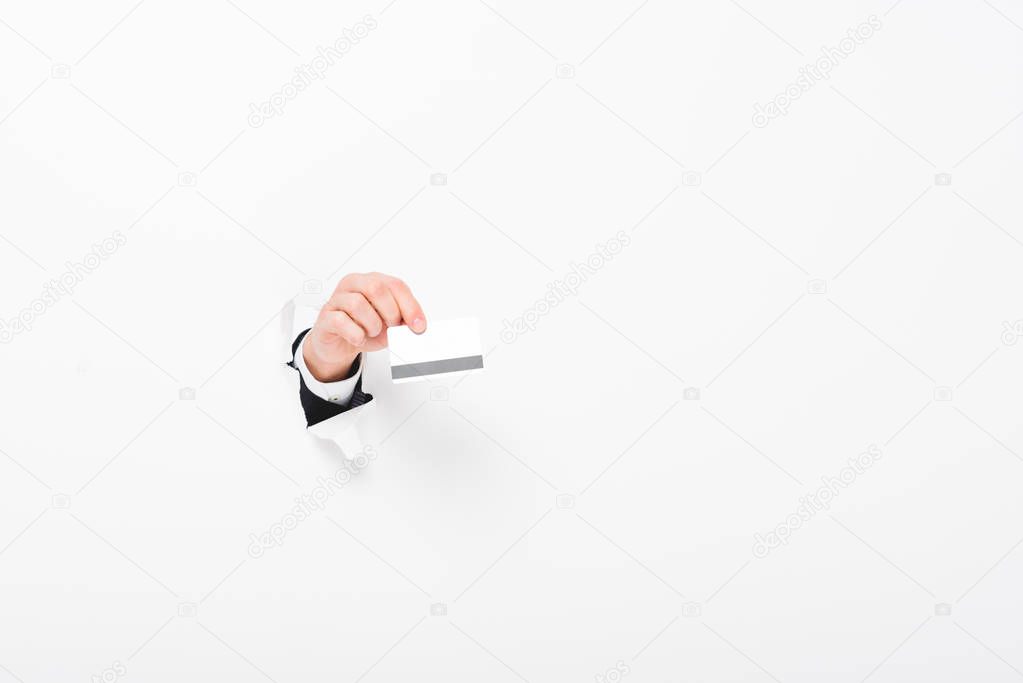 Cropped view of man holding Credit card from hole in wall on white with copy space