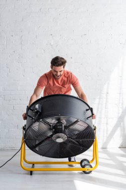 heyecanlı yakışıklı adam elektrik fan üfleme önünde beyaz duvarın yanında duran
