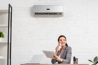 klima altında işyerinde otururken neşeli iş kadını içme suyu 