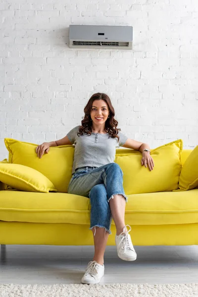 Schöne Lächelnde Frau Sitzt Auf Gelbem Sofa Unter Klimaanlage Hause — Stockfoto