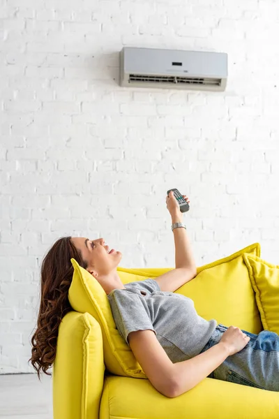Pretty Young Woman Lying Yellow Sofa Air Conditioner Holding Remote — Stock Photo, Image